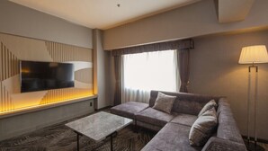 Una habitación de hotel moderna con sofá modular, un televisor de pantalla plana montado en la pared, una lámpara de pie y una alfombra estampada.