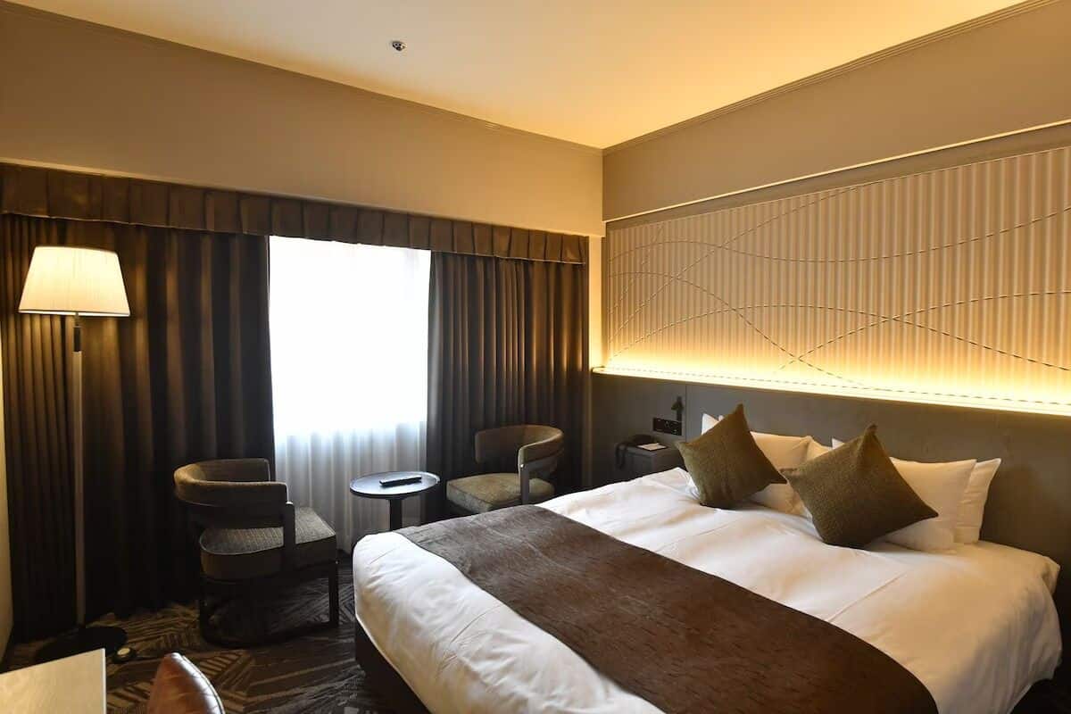 Une chambre d’hôtel avec un grand lit, deux fauteuils, une petite table et une lampe.