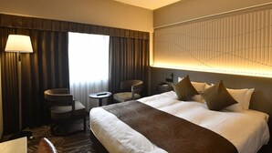 Una habitación de hotel con una cama grande, dos sillones, una mesita y una lámpara.
