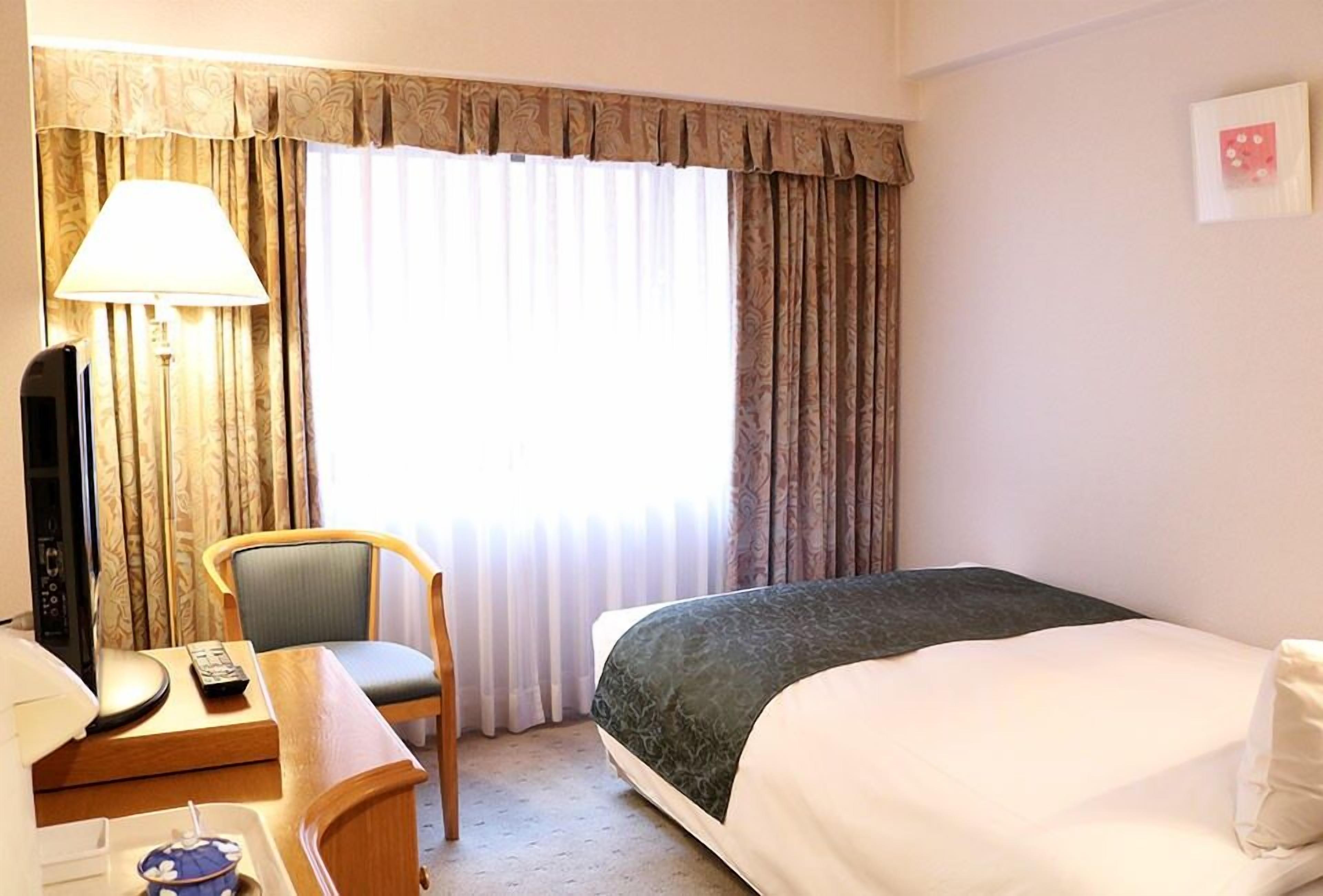 Une chambre d’hôtel avec un lit, un bureau doté d’une lampe, une chaise et un téléviseur.