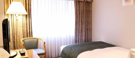 Une chambre d’hôtel avec un lit, un bureau doté d’une lampe, une chaise et un téléviseur.