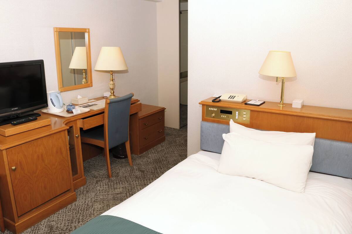 Une chambre d’hôtel équipée d’un lit, d’un bureau avec un ordinateur, d’une télévision, d’un téléphone et d’une lampe.