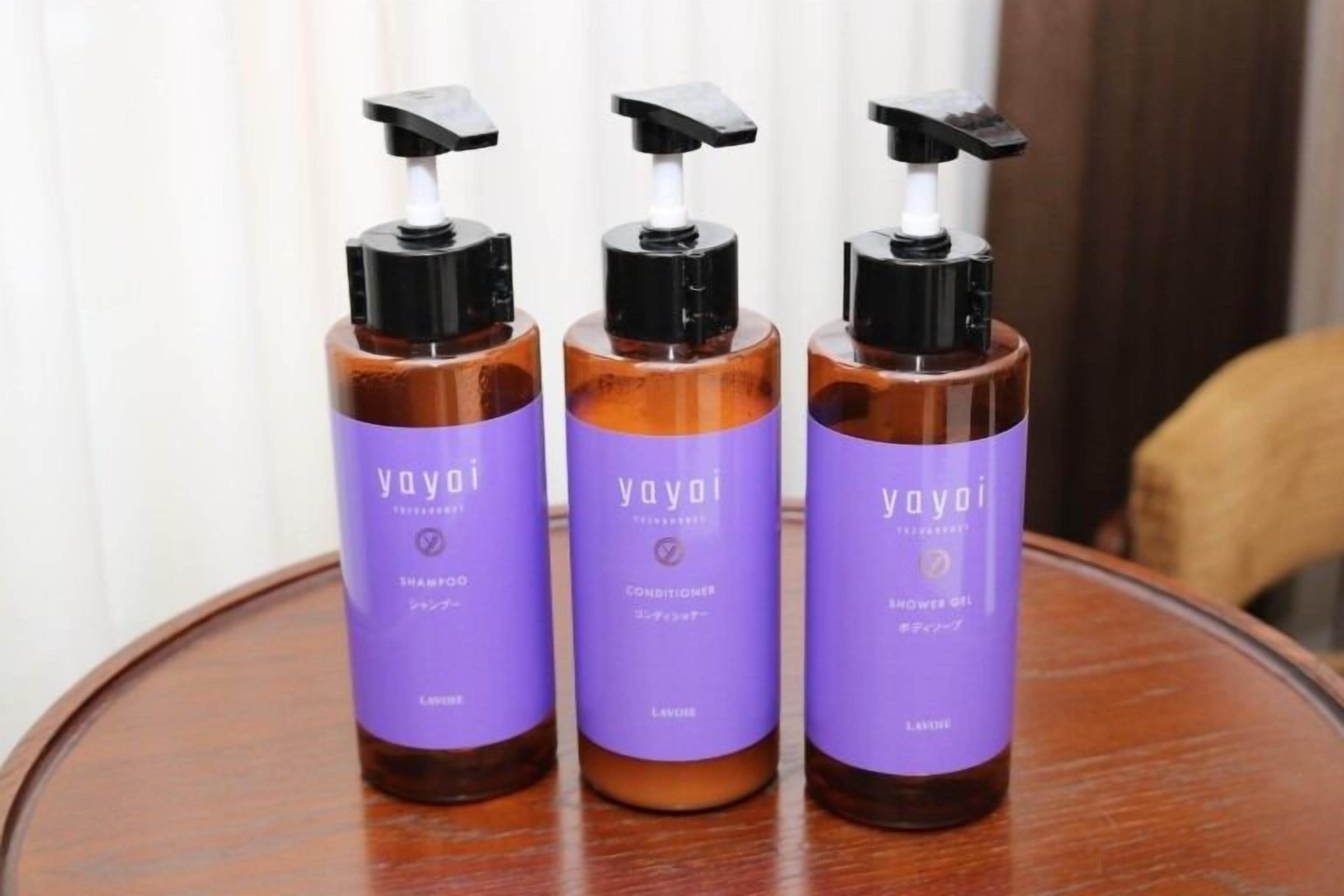 Tres botellas de champú, acondicionador y gel de ducha Yayoï sobre una mesa de madera.
