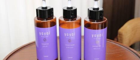 Tres botellas de champú, acondicionador y gel de ducha Yayoï sobre una mesa de madera.
