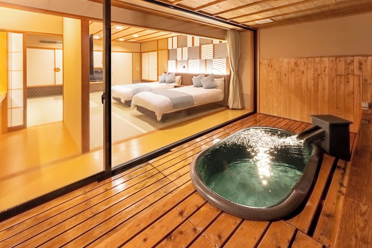 A traditional Japanese room with tatami flooring, a hot spring bath, and a sliding door leading to a bedroom with two beds.