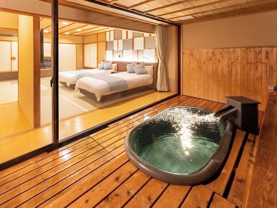 Een traditionele Japanse kamer met tatami vloeren, een thermaal bad en een schuifdeur naar een slaapkamer met twee bedden.
