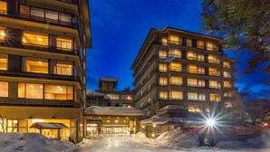 A multi-story hotel with a snow-covered entrance and illuminated windows. - Hotel Keisui (Omachi)