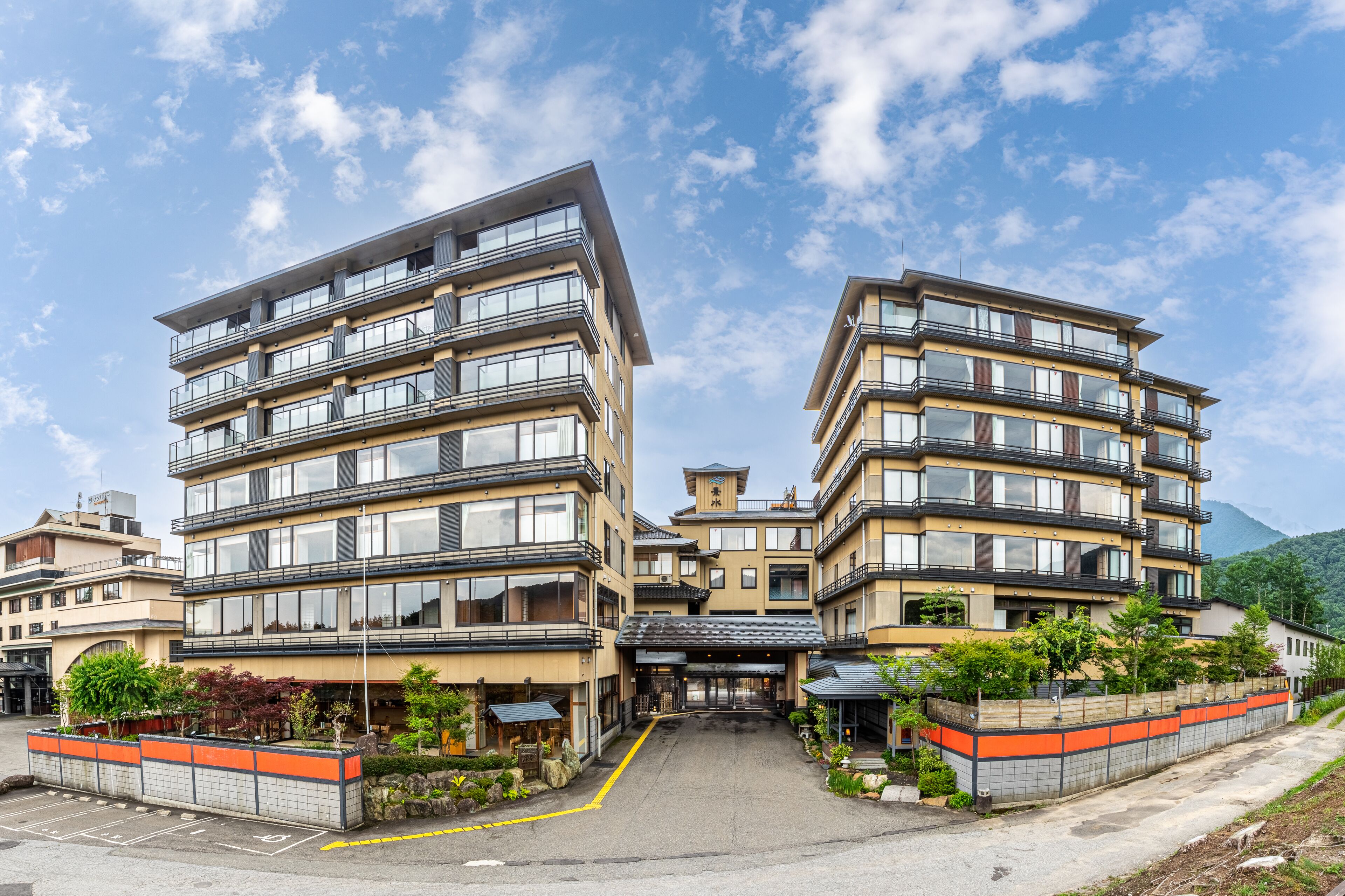 Ein modernes Mehrstöckiges Hotel mit zentralem Eingang, Außenbereich und Parkplatz.
