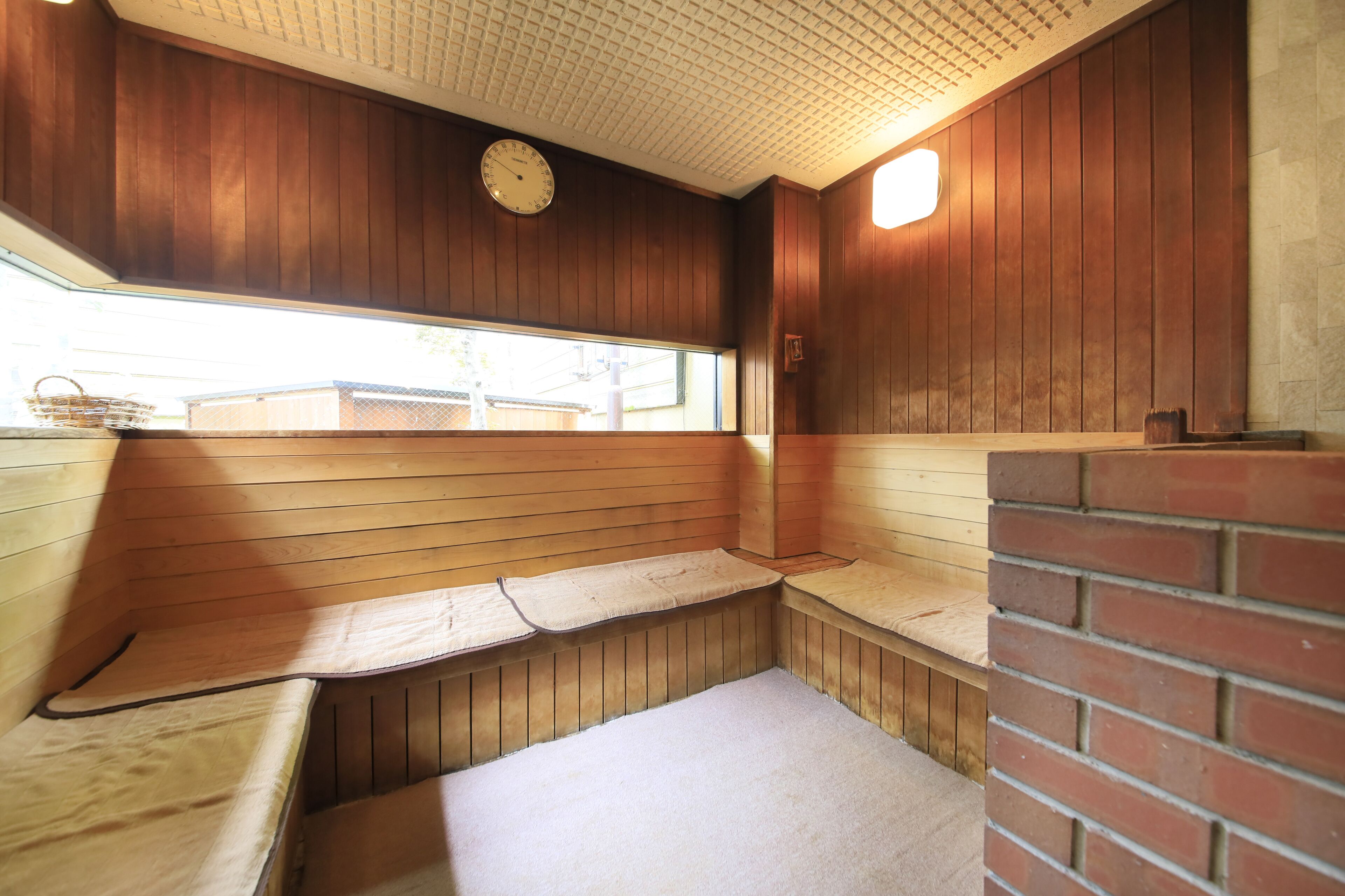 A sauna with wooden benches and a tiled floor, a clock on the wall, and a window with a view of the outside.