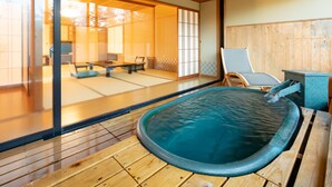 A traditional Japanese onsen with a wooden deck, a stone hot spring, and a view of a tatami room with furniture. - Hotel Keisui (Omachi)