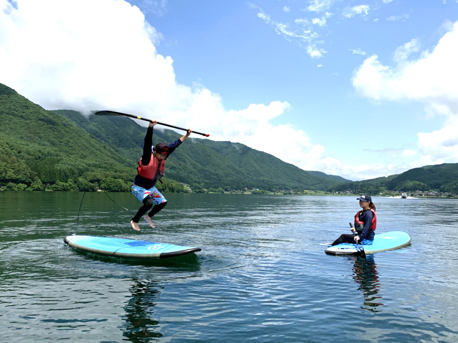 Two people on paddleboards in a calm lake with mountains in the background.