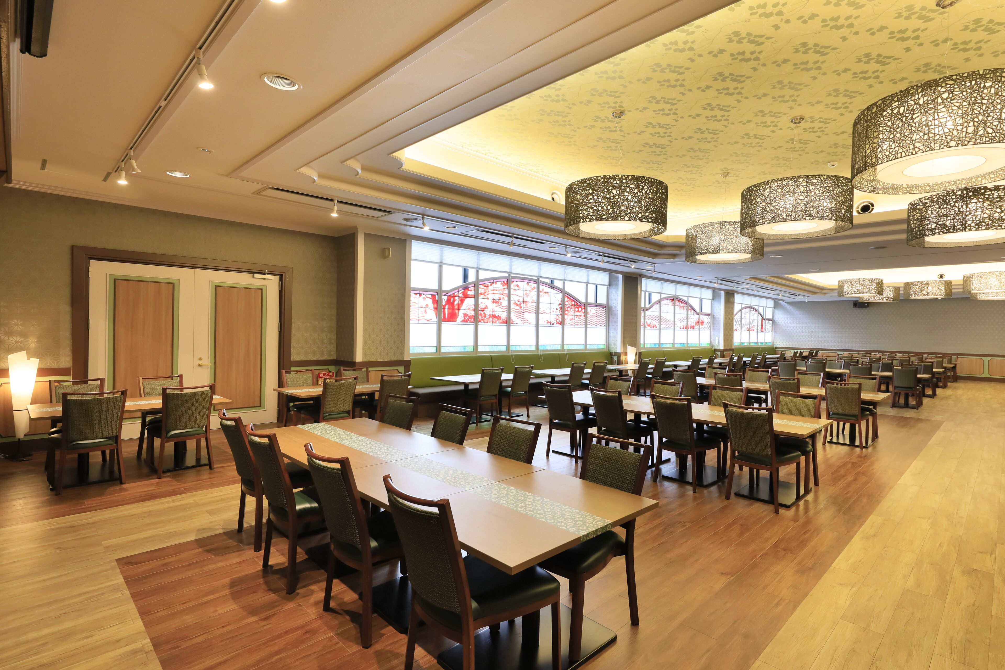 Una amplia sala de conferencias con varias mesas y sillas, ventanas grandes con vistas decorativas y luces de techo.