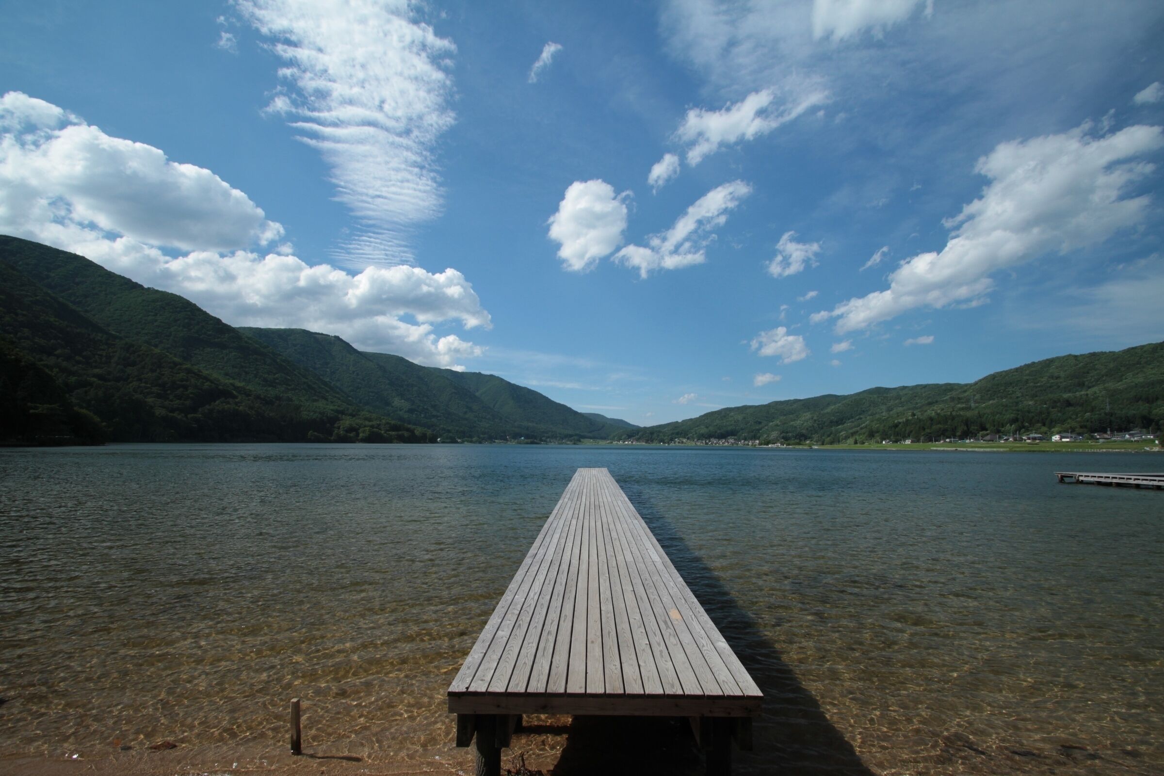 Un muelle de madera que se adentra en un lago tranquilo, rodeado de colinas verdes.