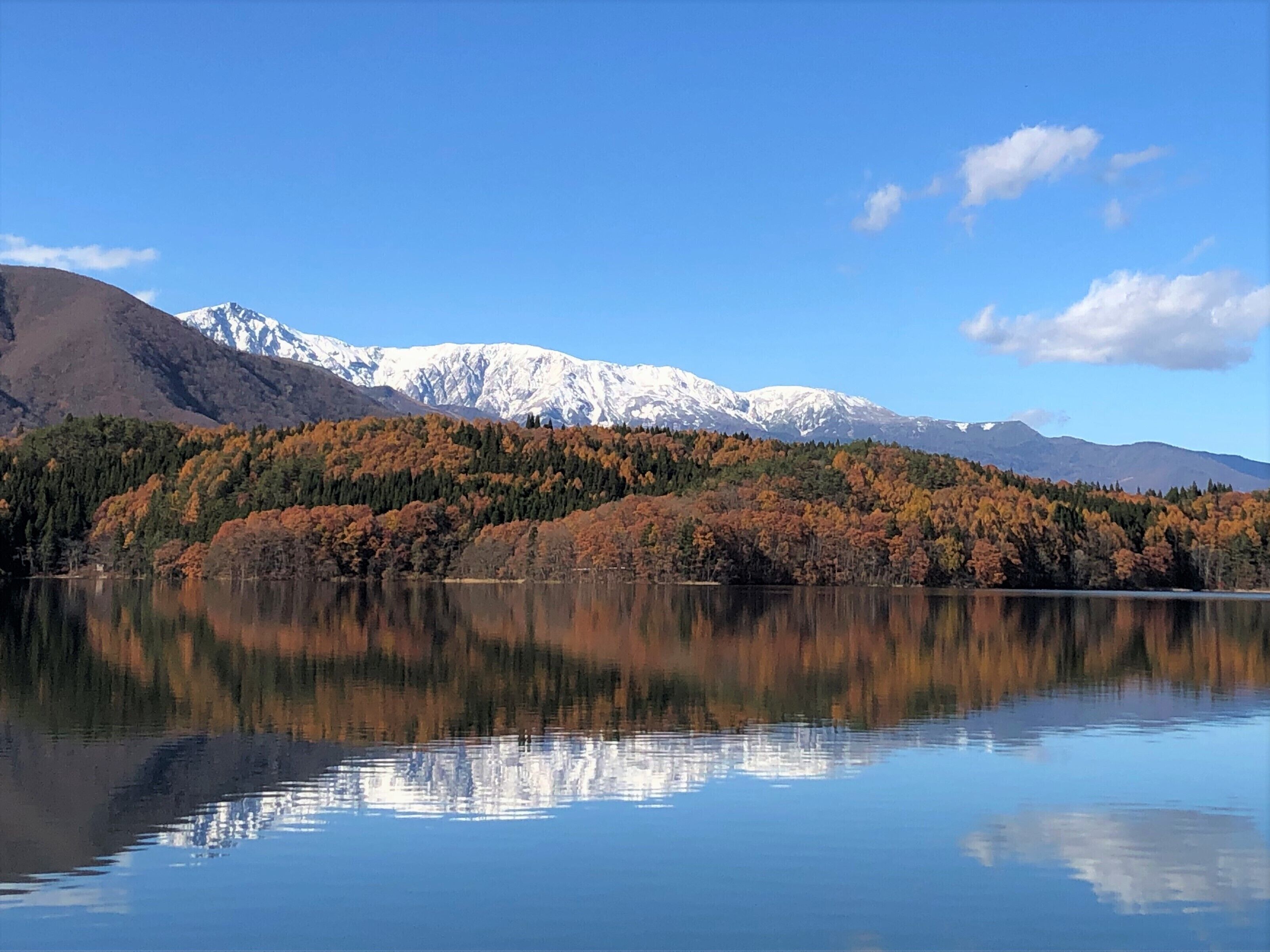 Un lago sereno que refleja un paisaje montañoso con follaje otoñal y cimas nevadas.