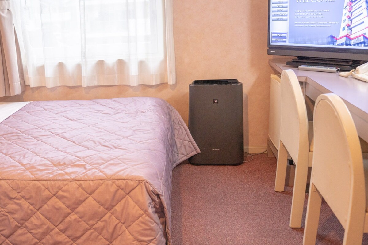 A hotel room with a bed, a desk with a computer, and a television.