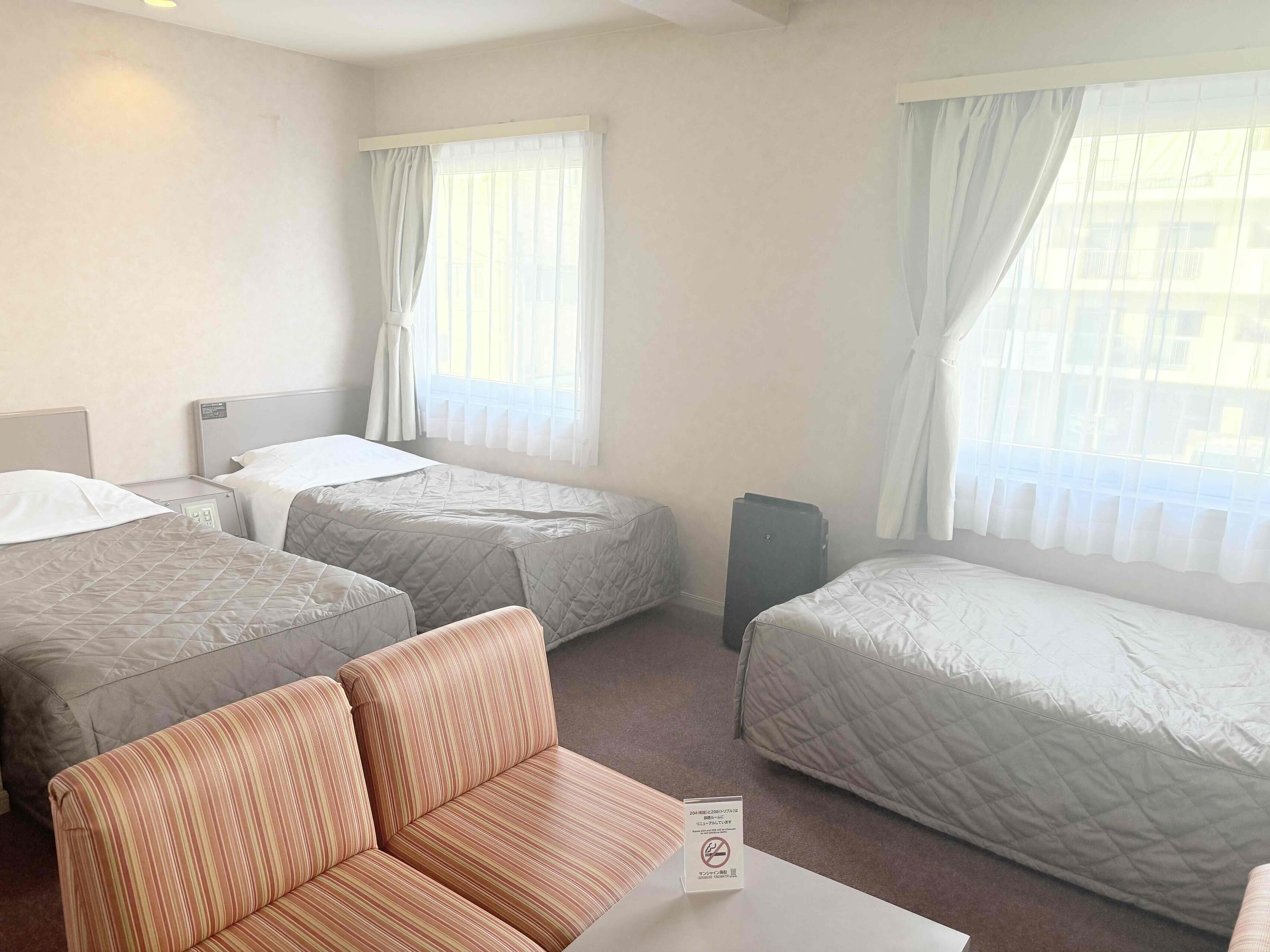 Quarto de hotel com duas camas, um sofá e uma pequena mesa.