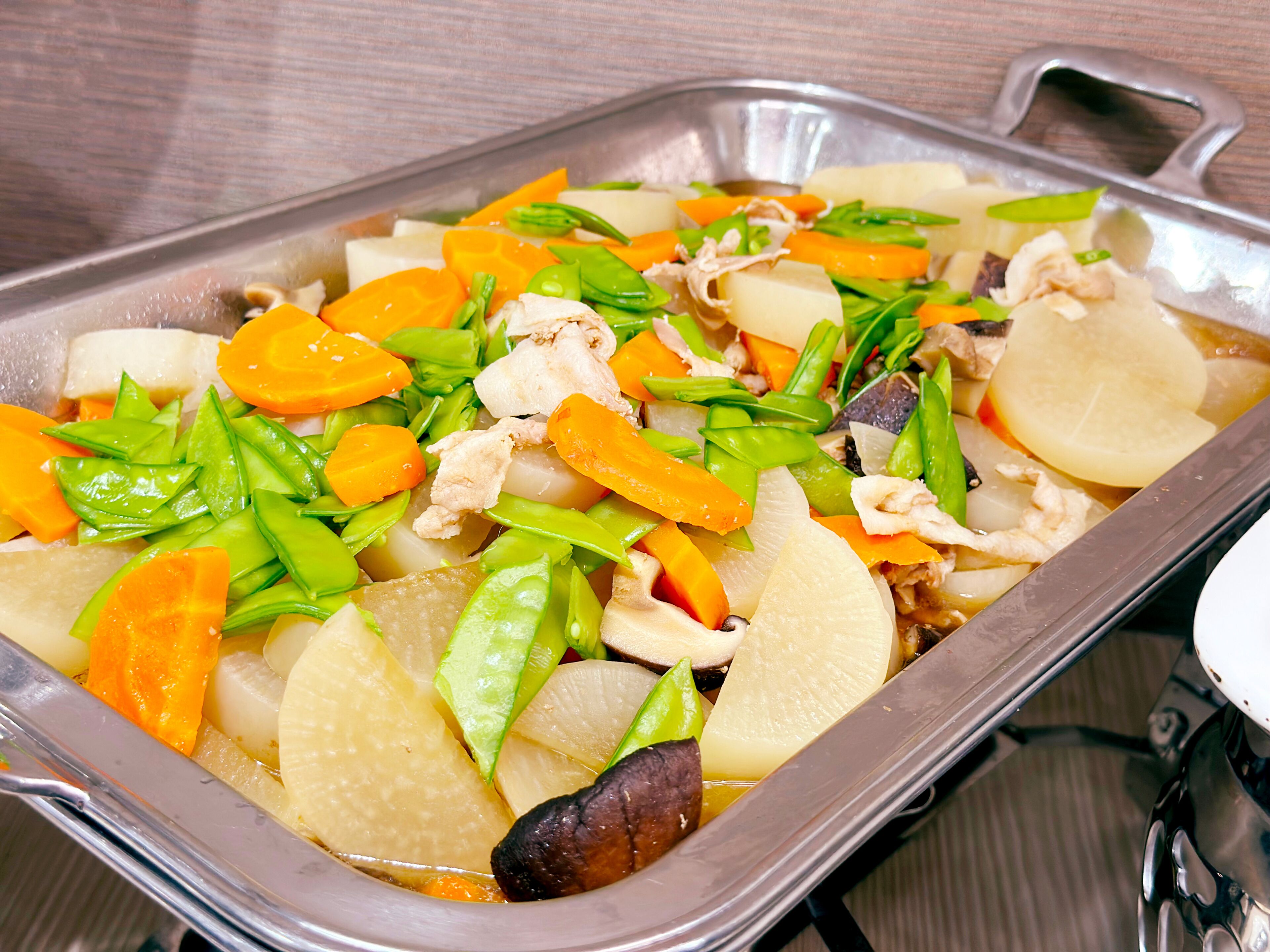 A stainless steel tray with sliced vegetables and meat, likely prepared for a meal.