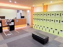 Zona de recepción con mostrador, computadora y señalización con indicaciones. Hay taquillas verdes y un banco acolchado negro.