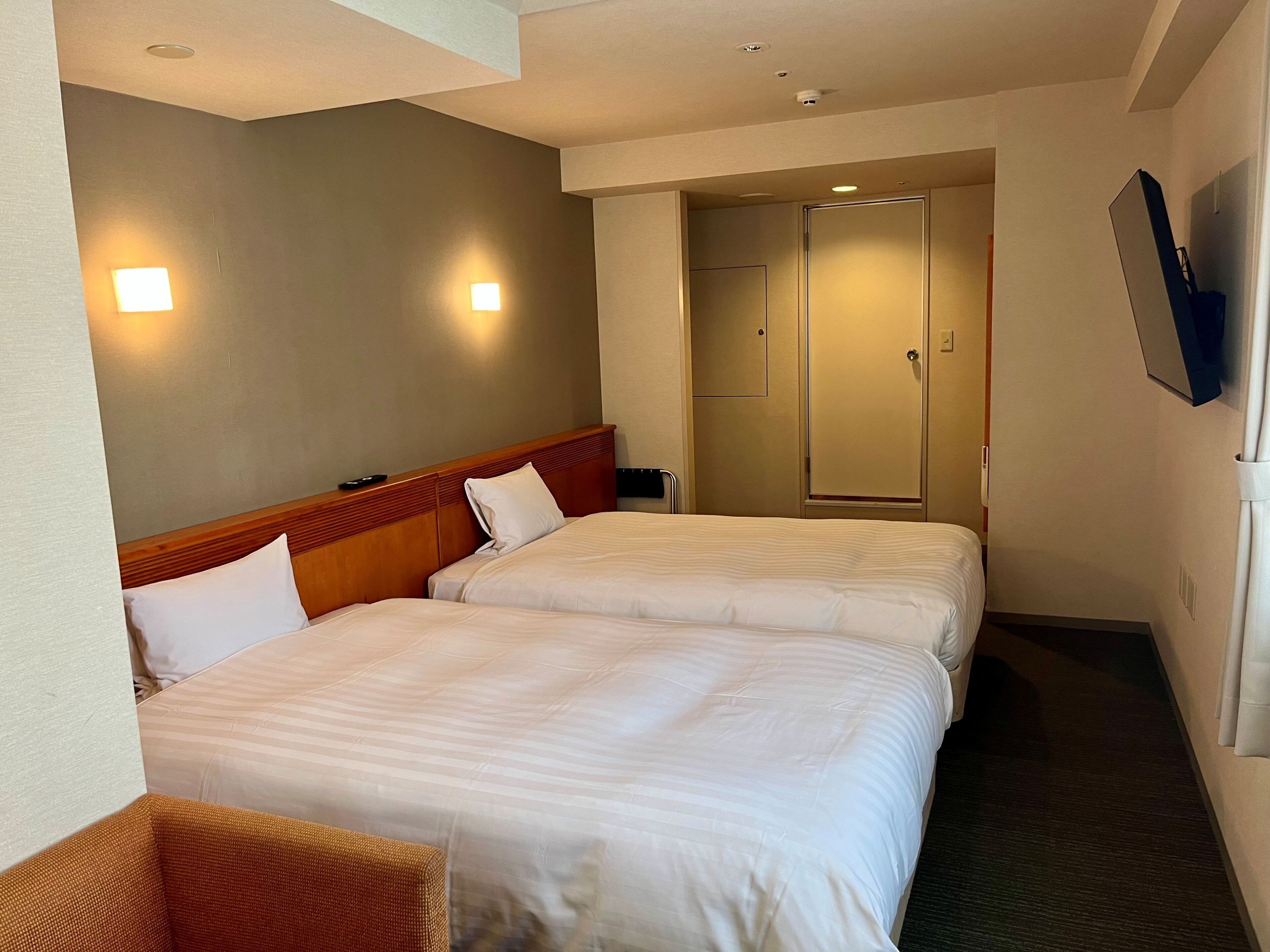 A hotel room with two beds, a television mounted on the wall, and a door leading to a bathroom.