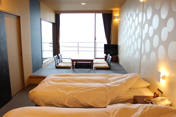 Habitación de hotel con dos camas, televisión, teléfono y ventana con cortinas.