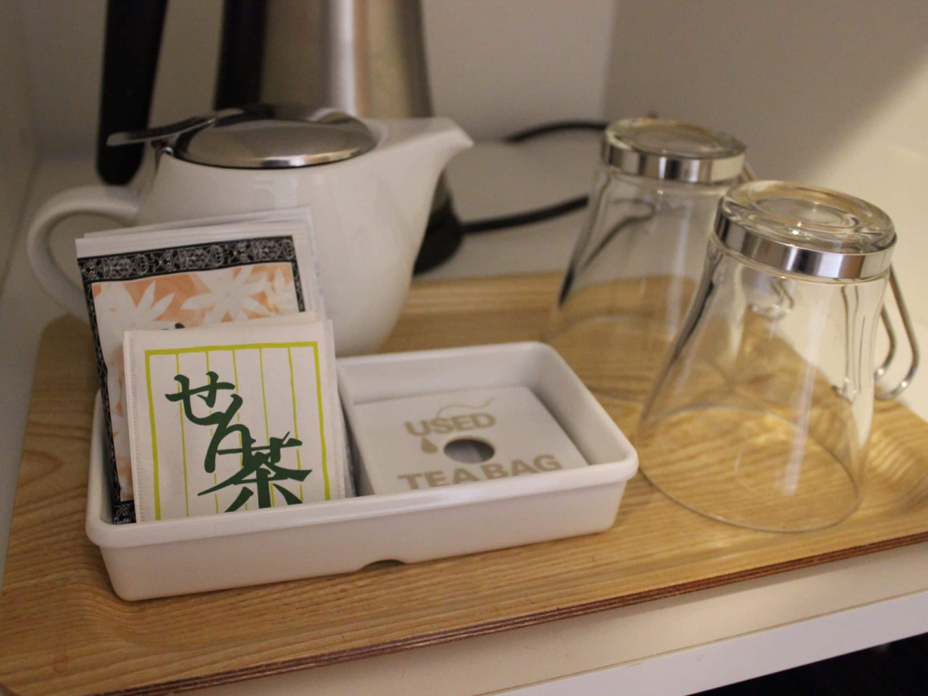A tray with a tea bag, a teapot, and a glass pitcher on a wooden surface.