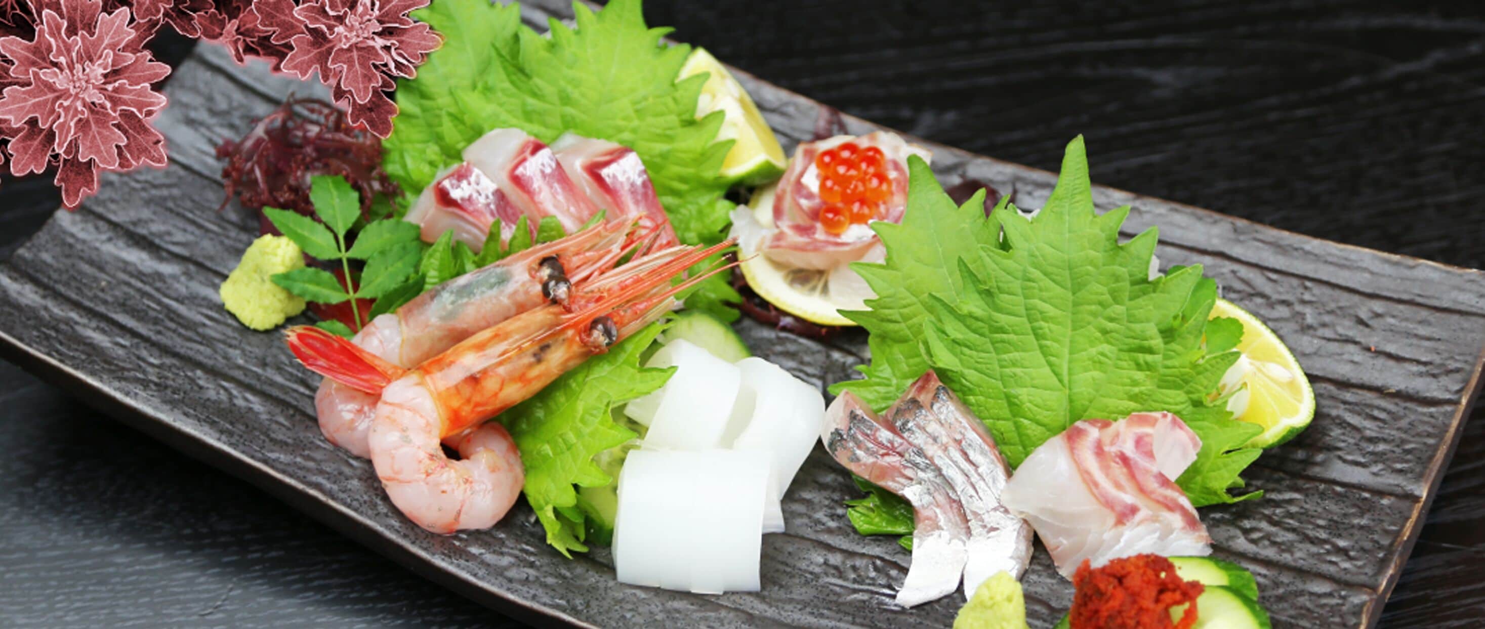 A seafood platter with shrimp, fish, and citrus on a slate plate.