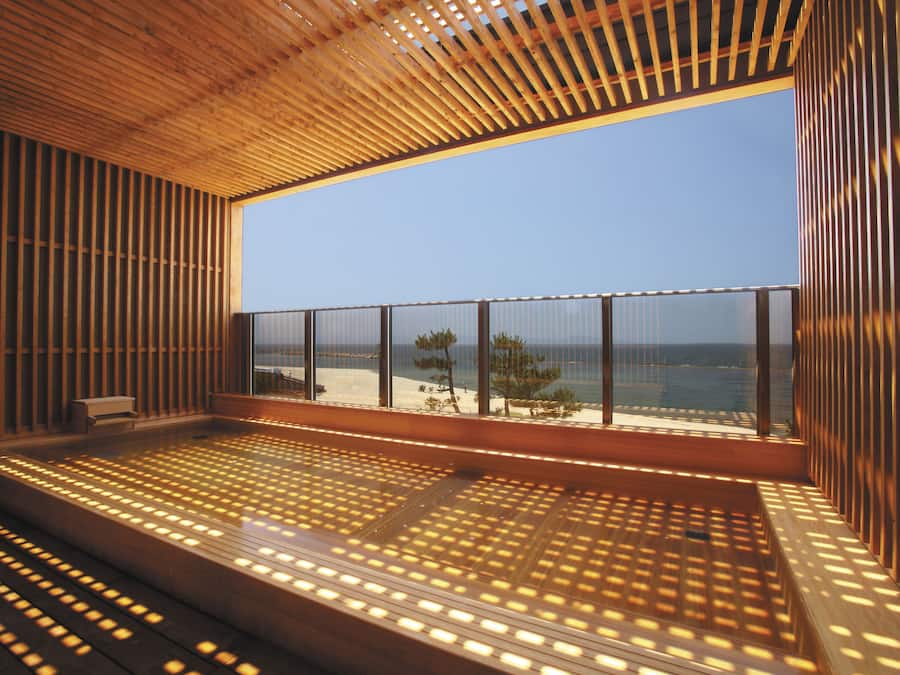 Un interior moderno con techo y suelo de listones de madera, y amplias ventanas que ofrecen vistas a la playa.