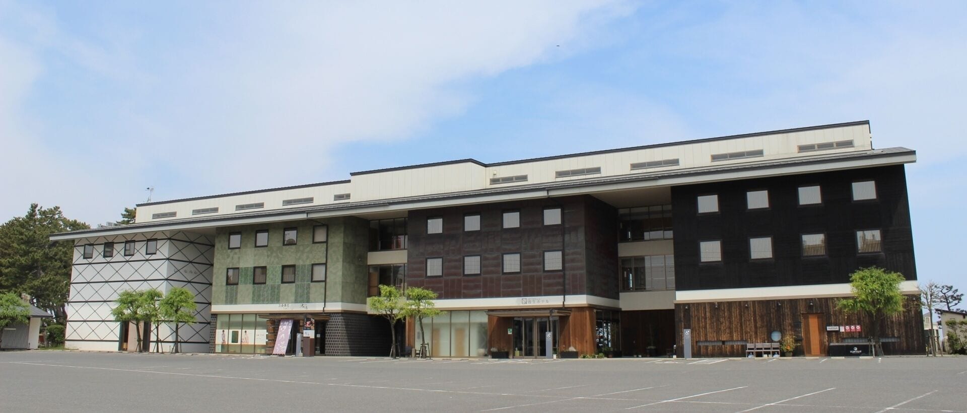 Un edificio moderno con techo plano, ventanas amplias y un estacionamiento al frente.