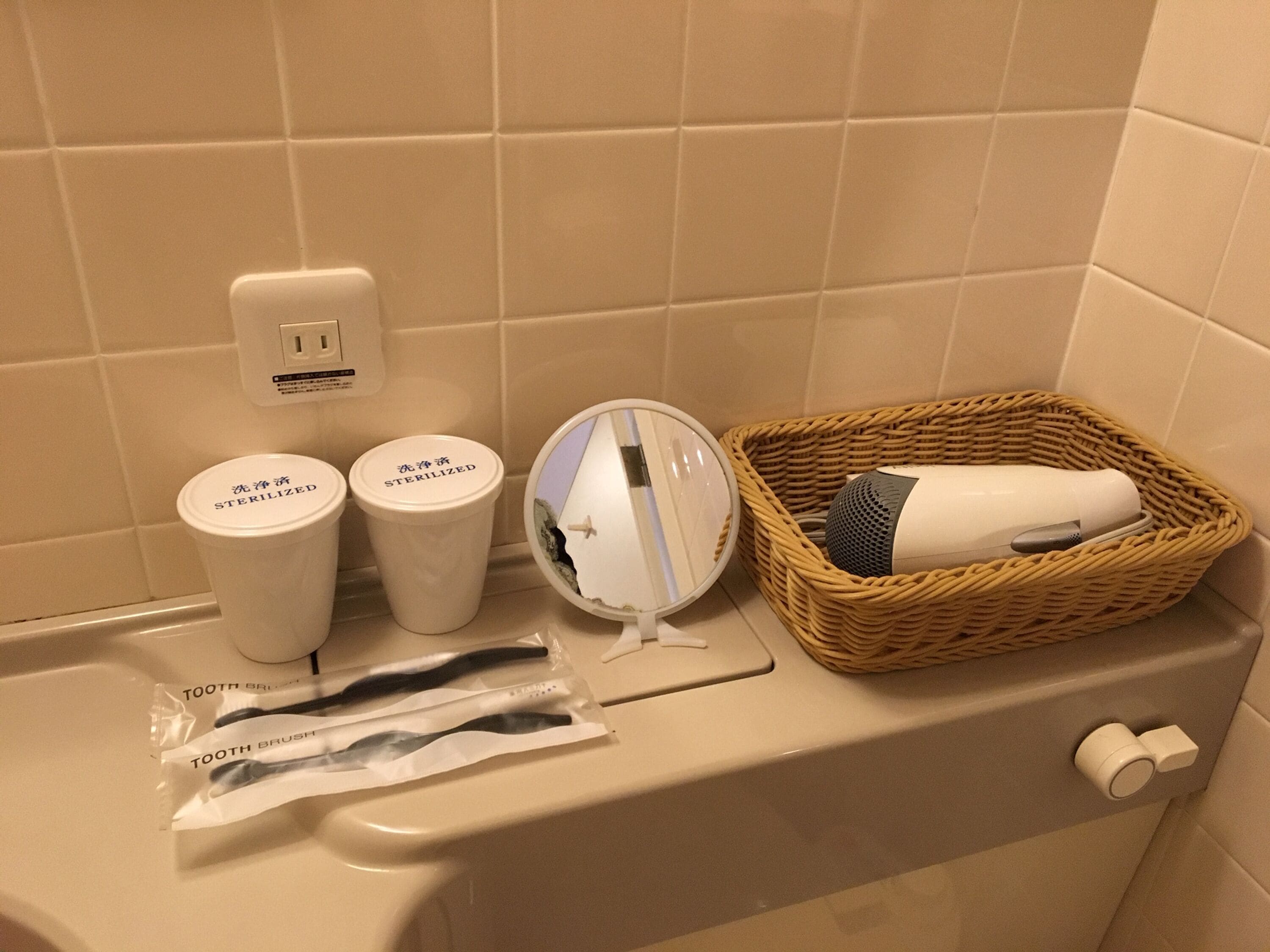 A bathroom with a white sink, toothbrushes, a hairdryer, and a toothbrush bag.
