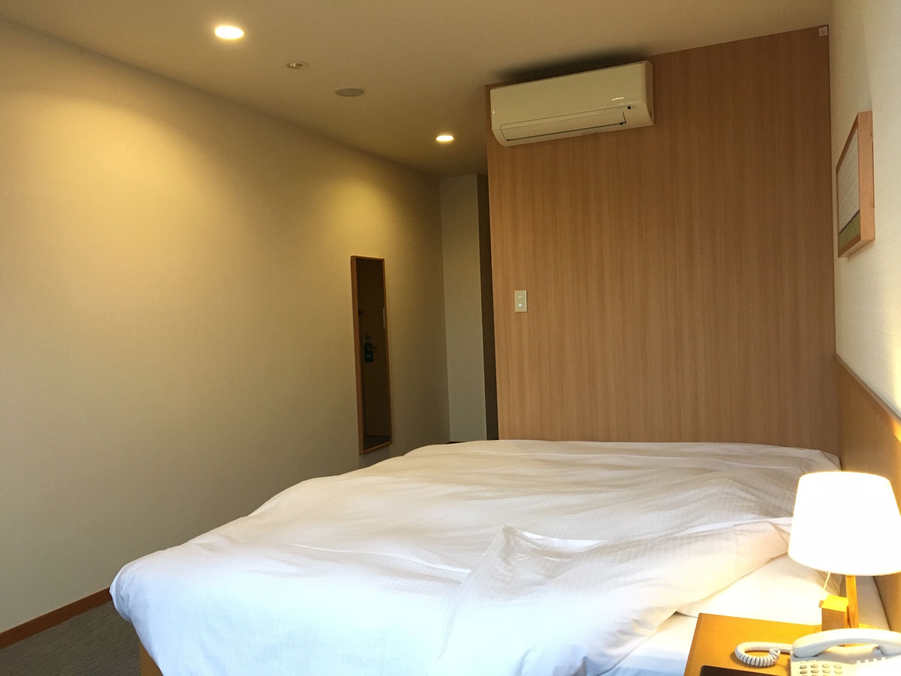 Habitación de hotel con cama, lámpara de noche, teléfono y aire acondicionado.