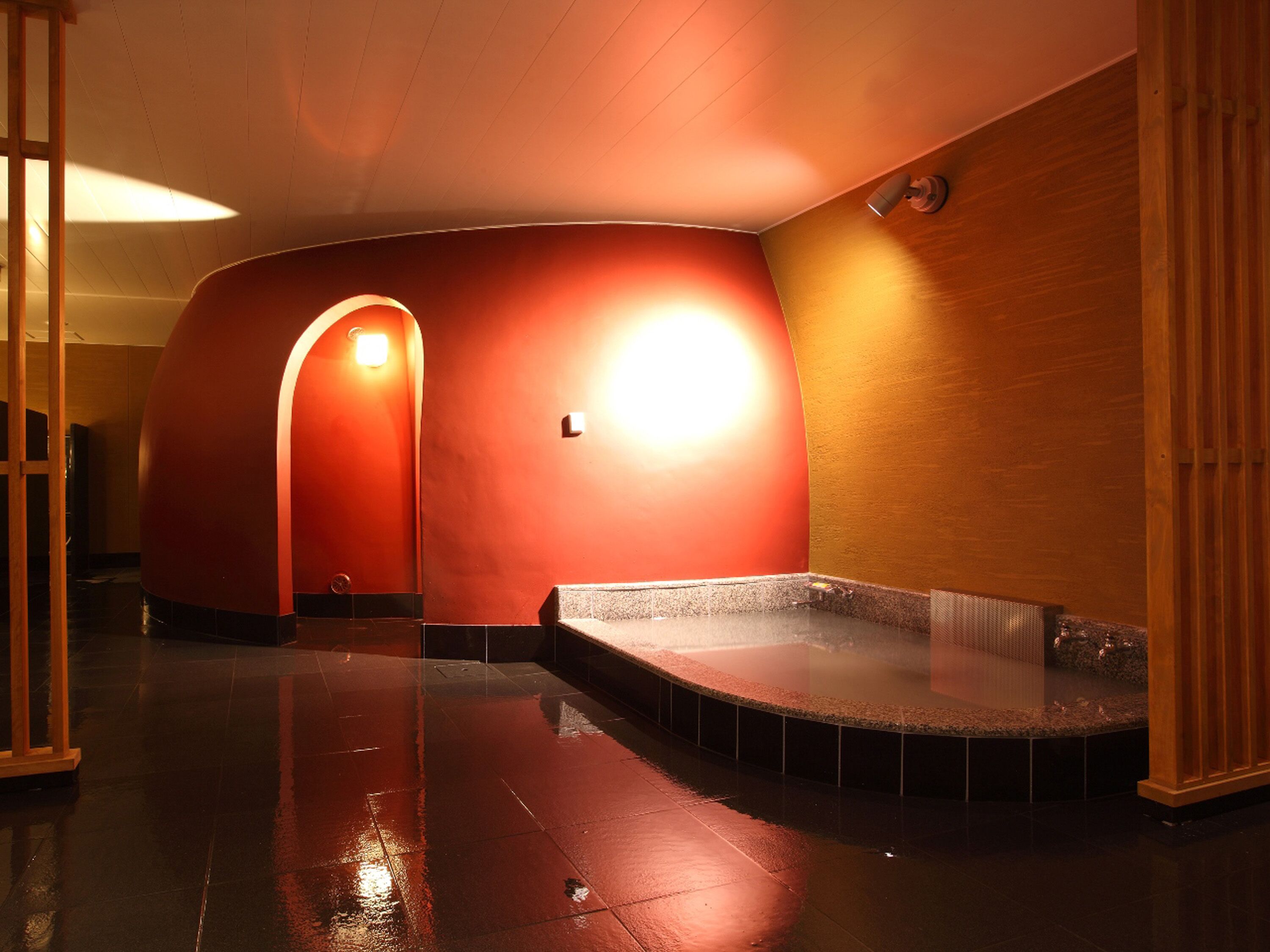 A modern, curved interior with a wet floor, a bench, and a wall-mounted light fixture.