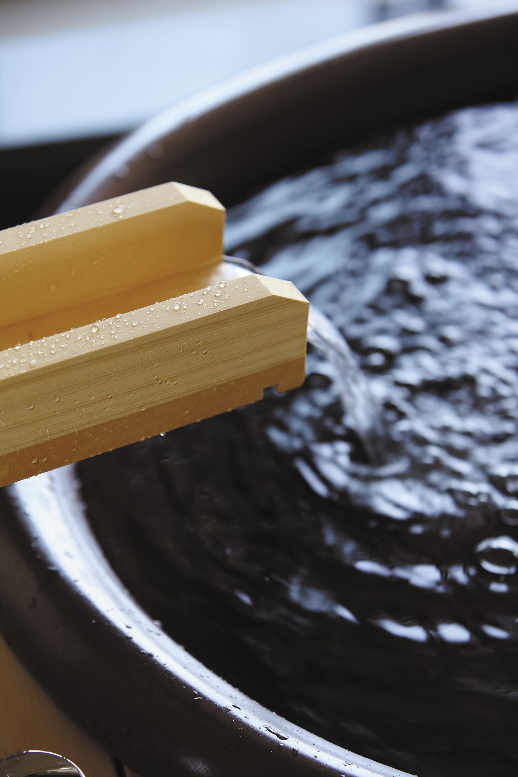 Un objeto de madera con gotas de agua, probablemente un palillo, sobre una superficie oscura de líquido.