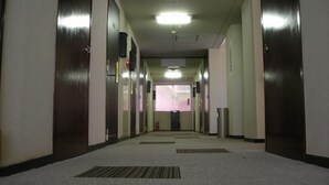 A corridor with doors on both sides, a fire extinguisher, and a trash bin. - Benefit Hotel Okayama 1 (Okayama)