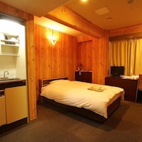 Una habitación con cama, escritorio, televisor y una kitchenette pequeña.