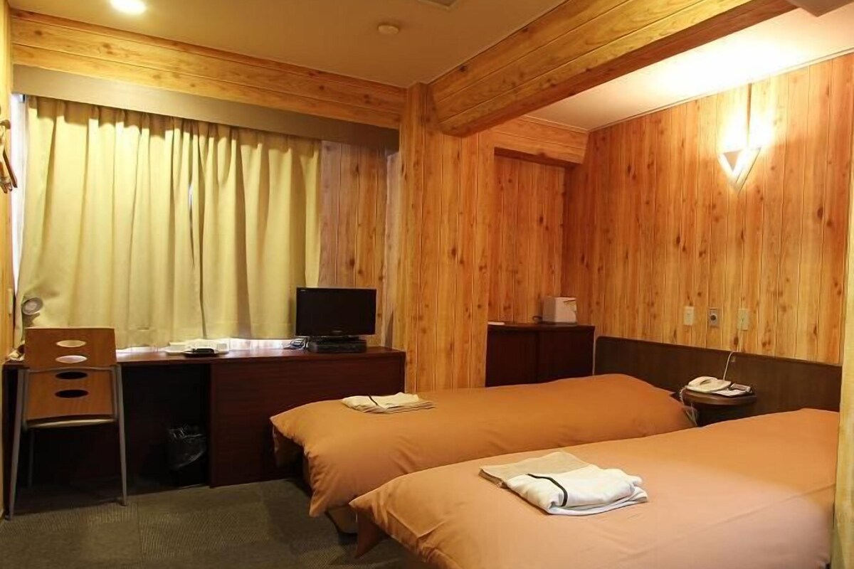 Habitación de hotel con dos camas, un escritorio, una silla, un televisor y paneles de madera.