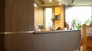 A reception desk with a wooden panel, a window with a view, and a counter with various items. - Benefit Hotel Okayama 1 (Okayama)