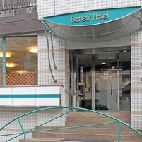 Entrada de un hotel con un letrero que dice 'Benefit Hotel', una puerta de vidrio y una escalera metálica que sube.