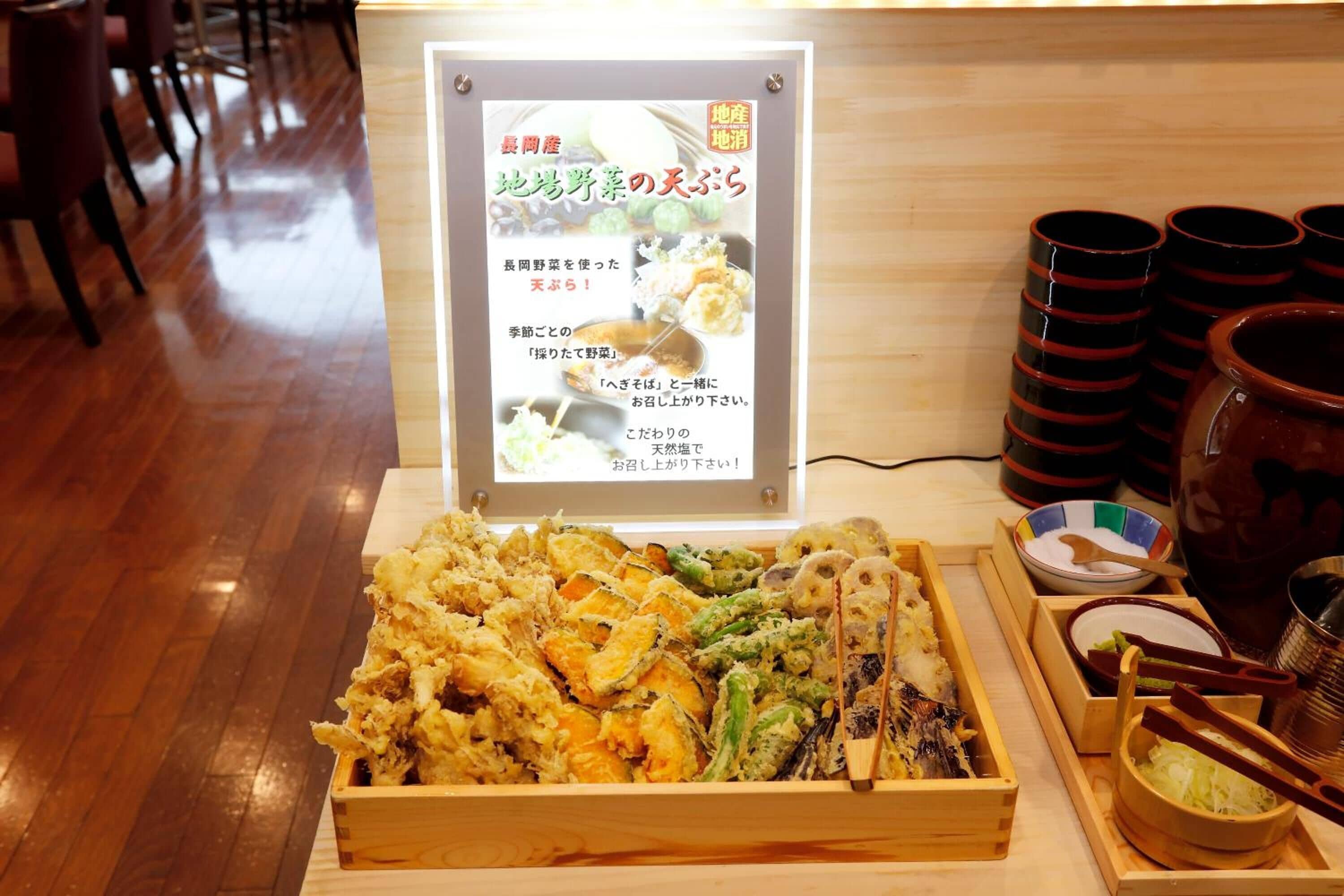 A wooden table with a variety of fried seafood and vegetables, a menu board, and stacked cups and bowls.