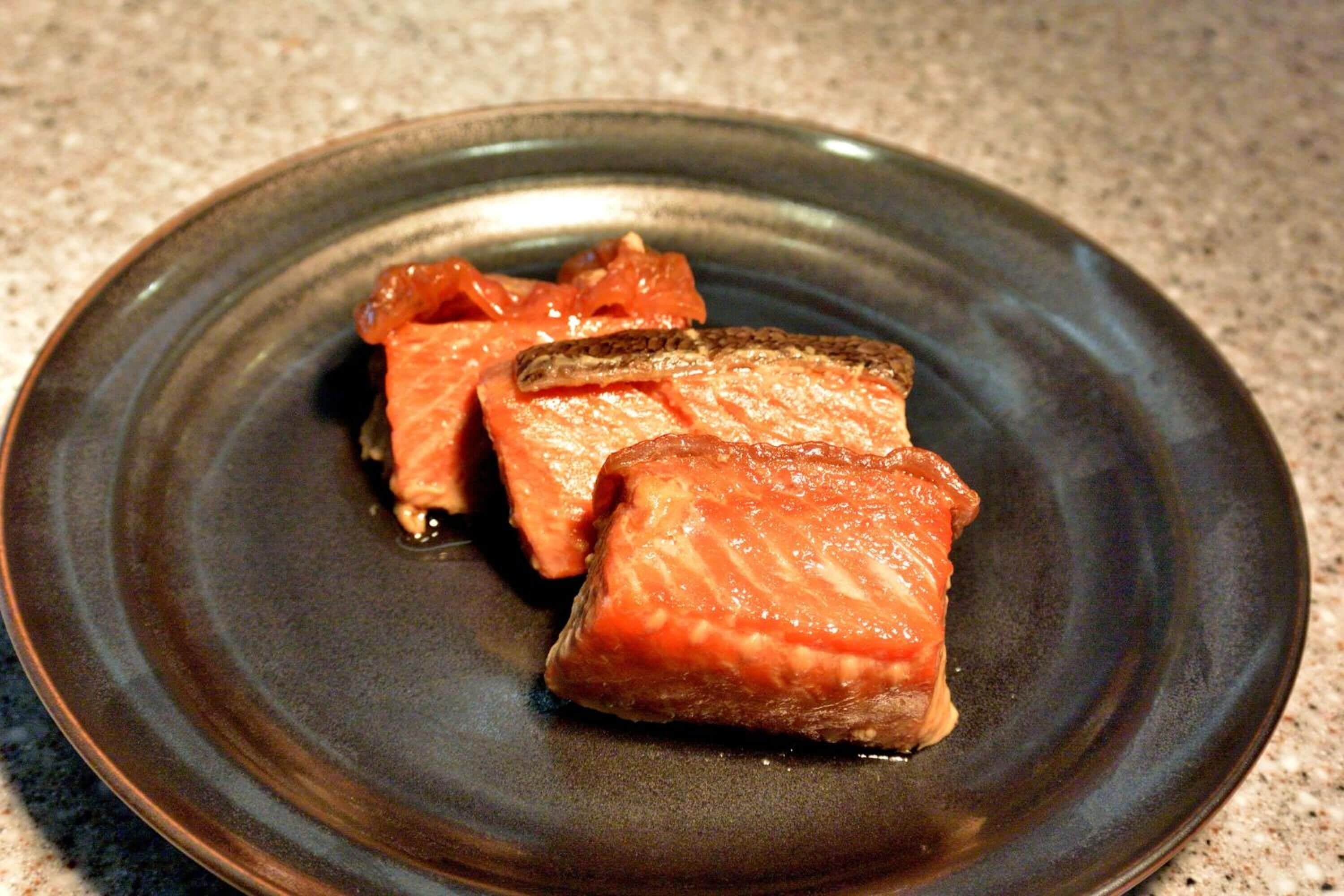 Une assiette en céramique foncée sur laquelle sont disposés des morceaux de saumon.