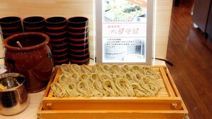 A wooden table with a tray of uncooked noodles, several black and red cups, and a brown pot.