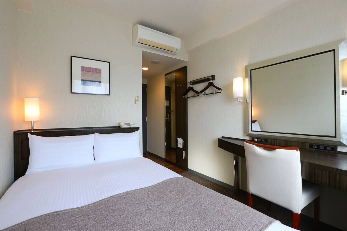 A hotel room with a large bed, bedside table, chair, and a mirror.