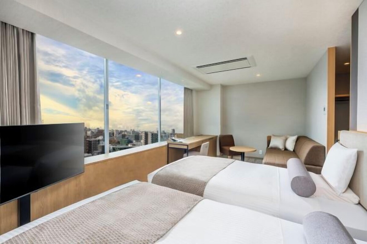 Una habitación de hotel con un ventanal grande, una cama, un escritorio y un televisor.