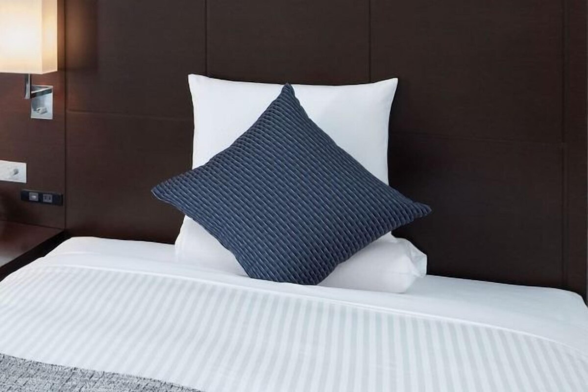 A neatly made bed with a white mattress and a dark blue pillow, set against a dark brown headboard.