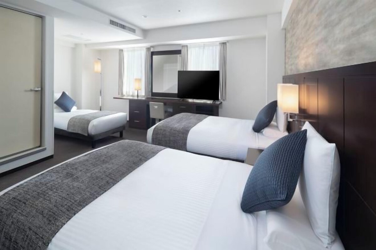 Habitación de hotel con dos camas, un escritorio, un televisor y un espejo grande.