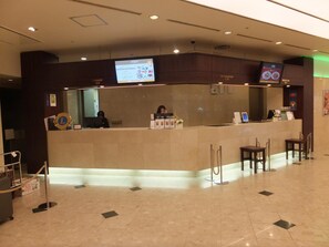 Zona de recepción de hotel con mostrador, pantalla digital y escritorio.