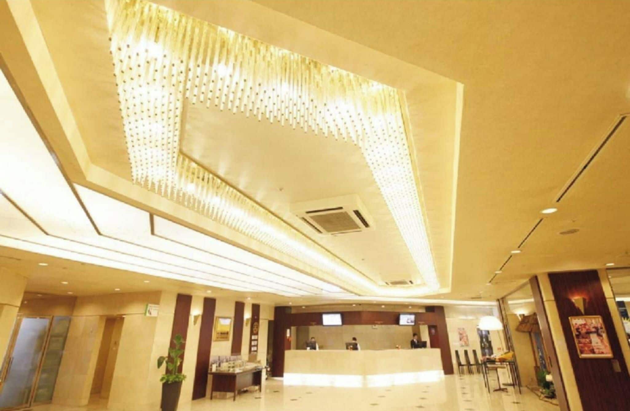 A hotel lobby with a reception desk, a large chandelier, and a modern ceiling design.