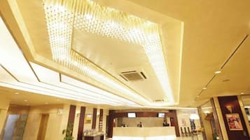 A hotel lobby with a reception desk, a large chandelier, and a modern ceiling design.