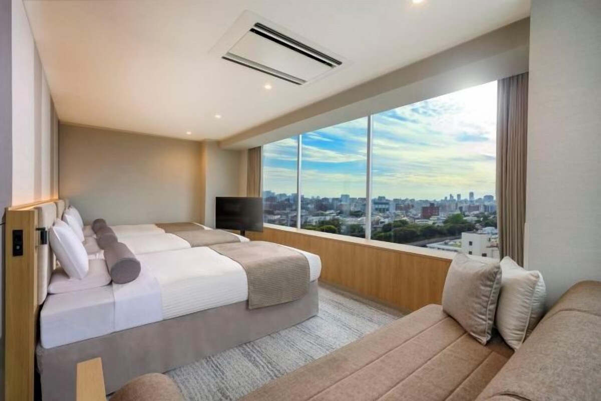 Una habitación de hotel moderna con una cama grande, un sofá y un televisor. La habitación tiene un ventanal con vistas a la ciudad.