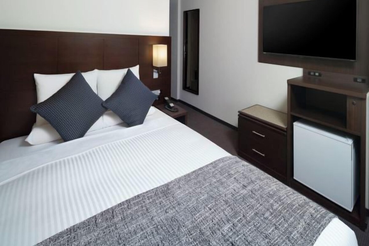 Una habitación de hotel con una cama grande, un televisor, un escritorio y un refrigerador pequeño.