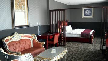 Ein Hotelzimmer mit einer roten, gepolsterten Couch, einem kleinen Tisch, einem Bett mit weißen Bettbezügen, einem Holzstuhl und einem Schreibtisch mit Stuhl.